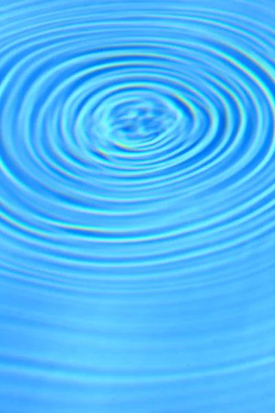 Sininen kirkas vesi pyöreä aaltoilu keskellä tausta — kuvapankkivalokuva