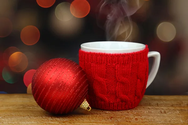 Christmas ball and hot drink in a cup in front of sparkle lights — Stock Photo, Image