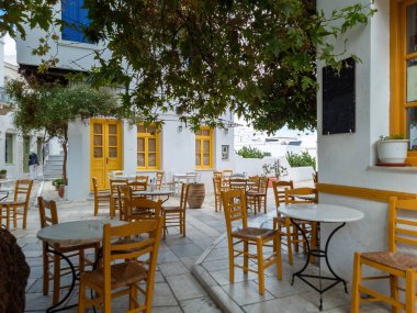 Pyrgos köyü Cyclades Yunanistan 'daki Tinos Adası' ndaki Yunan açık hava tavernası restoranı. Masalar, kaldırım taşına saman sandalyeler. Binalar arka plan, santraller.