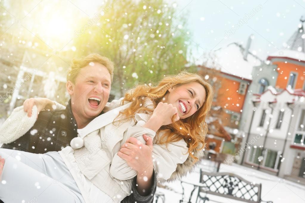 Winter couple piggyback in snow smiling happy and excited.