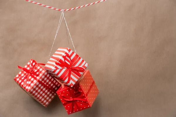 Red gift boxes hanging on a ribbon. Old brown paper background — Stock Photo, Image