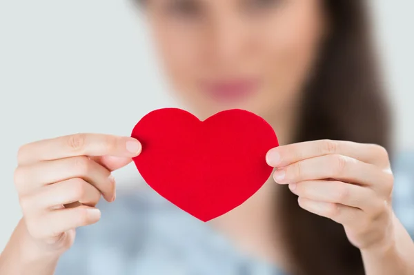 Joven mujer sonriente sosteniendo el corazón rojo. Concéntrate en corazón — Foto de Stock