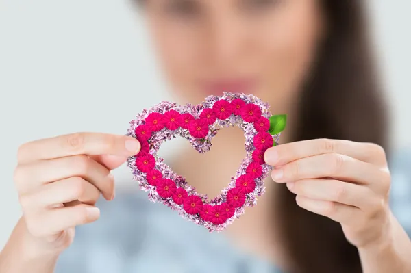 Joven mujer sonriente sosteniendo un corazón rojo hecho de flores. Concéntrate en corazón — Foto de Stock