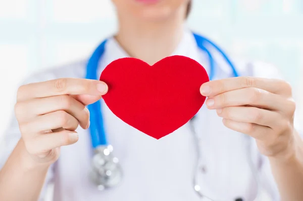 Doctora con estetoscopio sosteniendo el corazón humano rojo — Foto de Stock