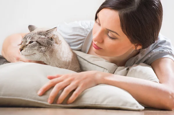 Een aantrekkelijke vrouw en haar kat ontspannen op kussens op de vloer — Stockfoto