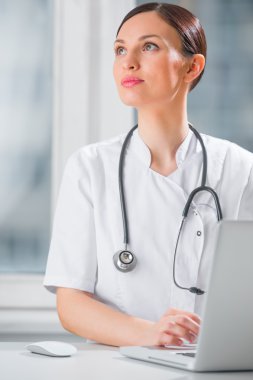 Klinikte dizüstü bilgisayarını kullanan bir kadın doktorun portresi.