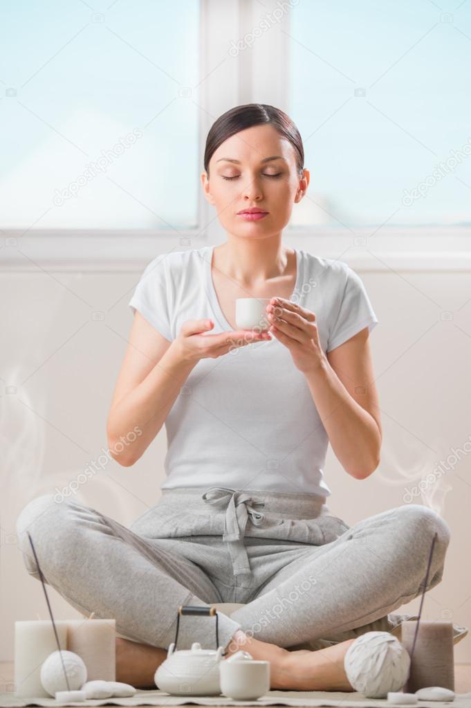 Young woman holding cup of tea or coffee at home and breathing