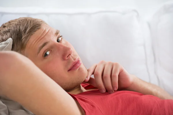 Portrait of a happy young man laying on sofa in thought — Stock Photo, Image