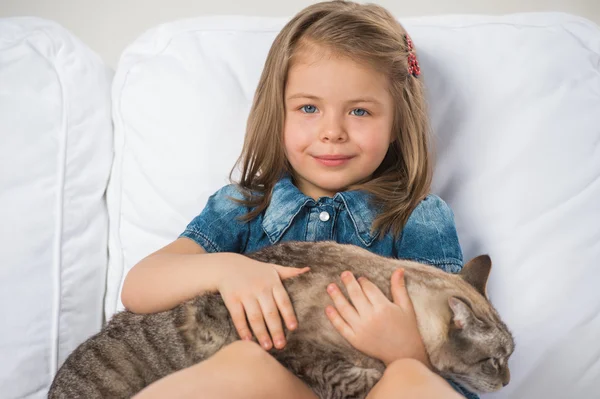 Söt liten flicka kramar tabby katt med kärlek, titta på kameran. — Stockfoto