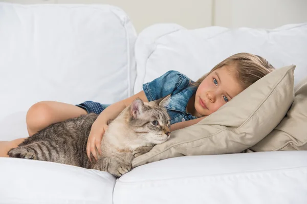 Маленька дівчинка лежить на дивані зі своєю таббі кішкою — стокове фото