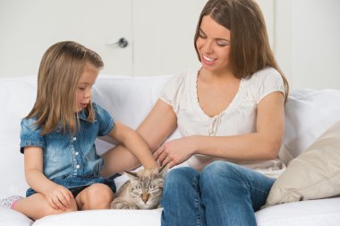 Anne ve kızı koltukta oturan ve kedi sarılma