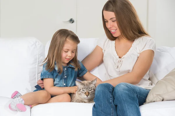 Mother and daughter sitting on sofa and cuddling cat — Stock Photo, Image
