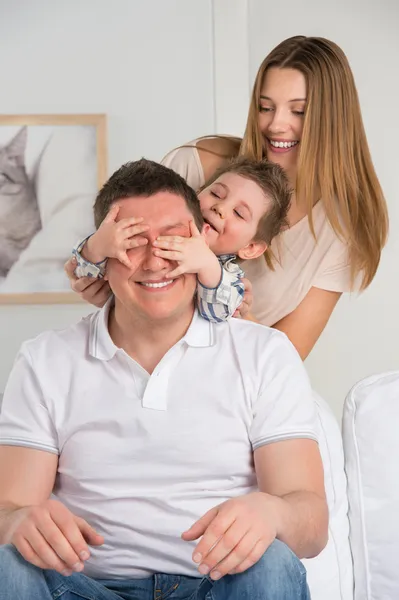 Happy family having fun in the living room: son surprisng his father by covering his eyes — Stock Photo, Image