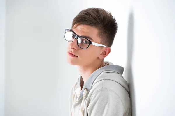 Porträt eines jungen modischen Mannes, der sich an eine weiße Wand lehnt und eine Brille trägt — Stockfoto