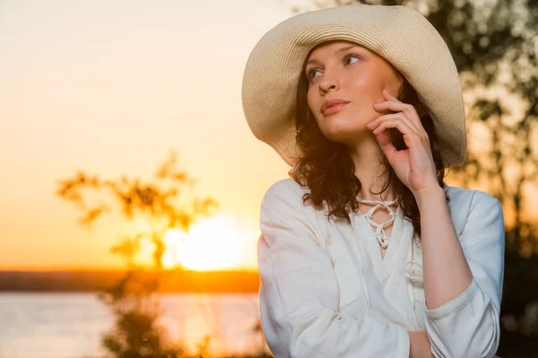 Mujer joven y hermosa usando un sombrero en la luz del atardecer — Foto de Stock