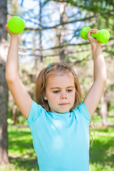 Feliz niña levantando pesas en el parque al aire libre — Foto de Stock