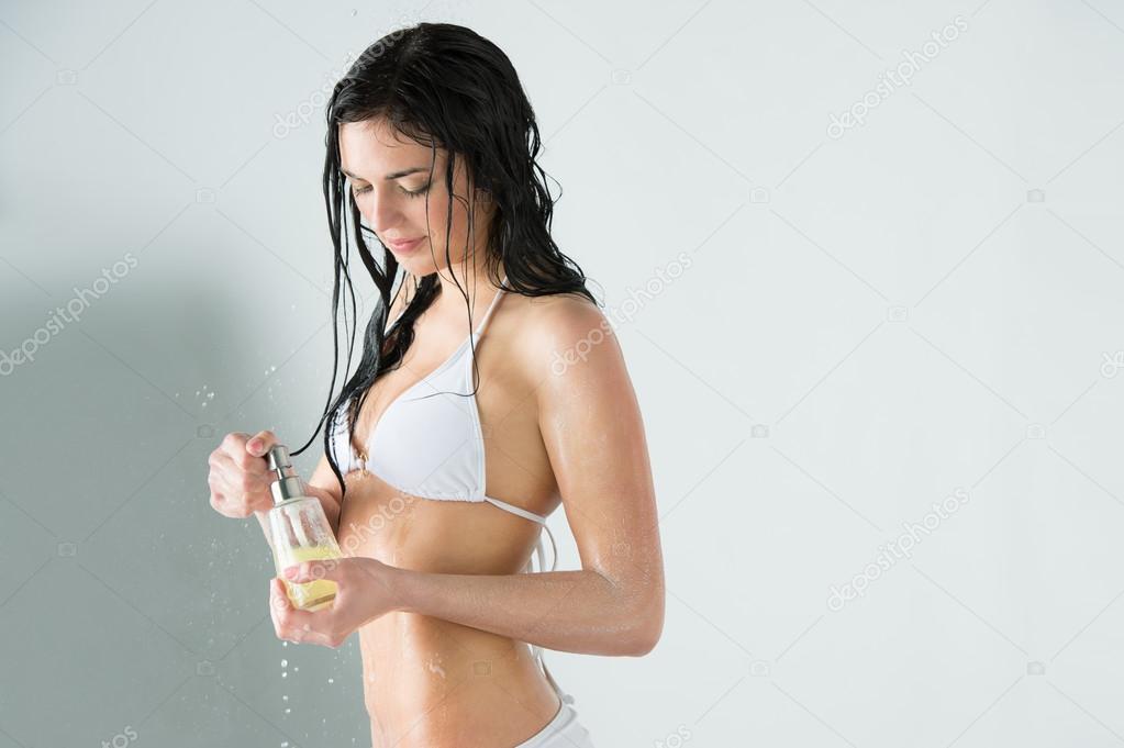 Beautiful girl showering. Holding glass bottle with shower gel