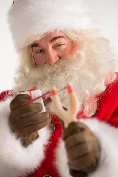 Porträt eines glücklichen Weihnachtsmannes, der mit Schleuder auf ein Weihnachtsgeschenk zielt — Stockfoto