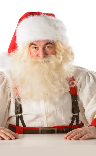 Weihnachtsmann sitzt am Tisch und blickt in die Kamera — Stockfoto