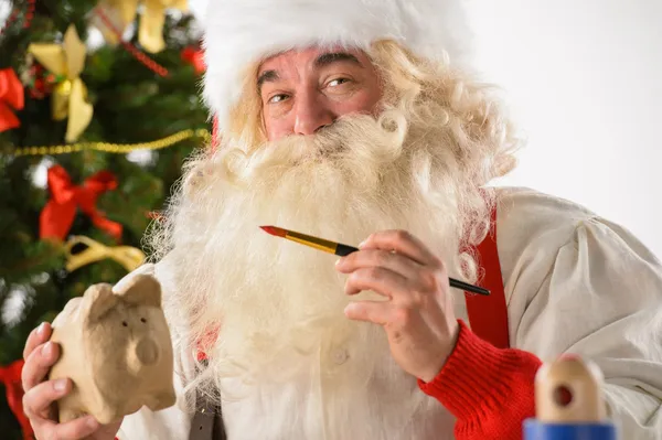 Authentic Santa Claus holding piggy bank and painting it — Stock Photo, Image