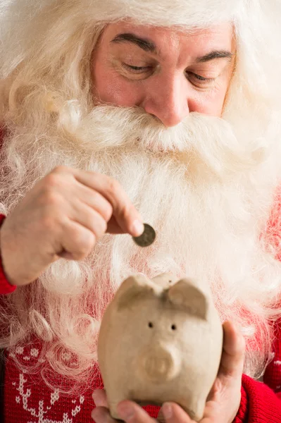 Authentic Santa Claus holding piggy bank and putting golden coin