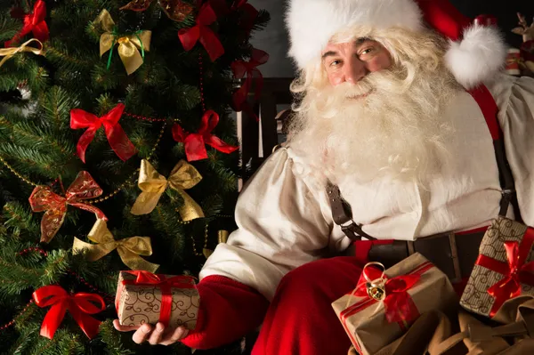 Санта кладет подарки под елку в темной комнате — стоковое фото
