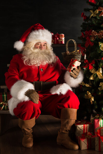 Санта кладет подарки под елку в темной комнате
