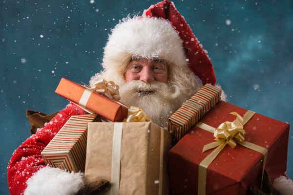 Фото счастливого Санта-Клауса на улице в снегопаде с подарками т
