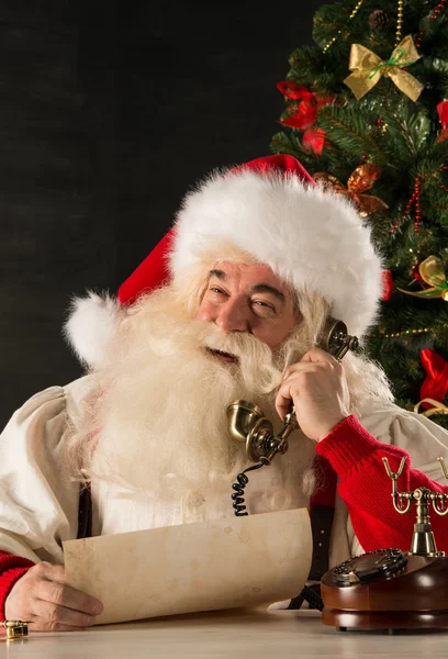 Santa Claus calling with vintage phone while reading an old roll — Stock Photo, Image