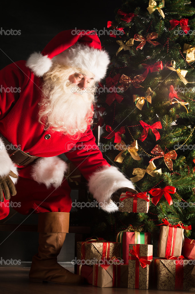 Santa putting gifts under Christmas tree in dark room — Stock Photo © HASLOO 32363175