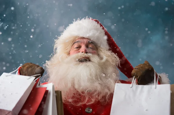 Santa claus buitenshuis in sneeuwval houden shopping tassen — Stockfoto