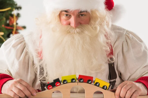 Weihnachtsmann sitzt und spielt mit Eisenbahnspielzeug — Stockfoto