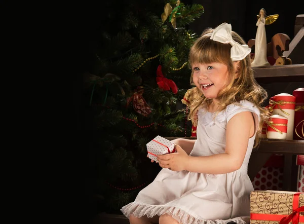 Szczęśliwa dziewczynka z prezenty, siedzący obok choinki — Zdjęcie stockowe