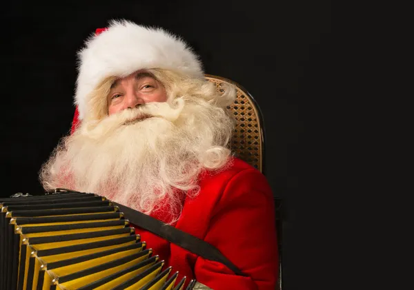 Jultomten sitter i fåtölj hemma och spelar musik på dragspel — Stockfoto