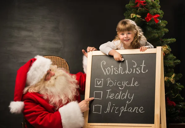 Santa Claus con niño sentado cerca de pizarra con lista de deseos —  Fotos de Stock