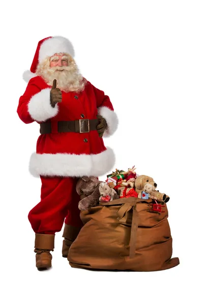 Santa Claus posando cerca de una bolsa llena de regalos y pulgares hacia arriba — Foto de Stock