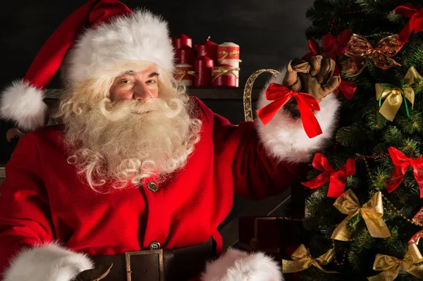 Weihnachtsmann schmückt Weihnachtsbaum im dunklen Raum — Stockfoto