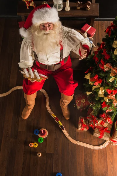 Papai Noel em casa brincando com novos brinquedos perto da árvore de Natal — Fotografia de Stock