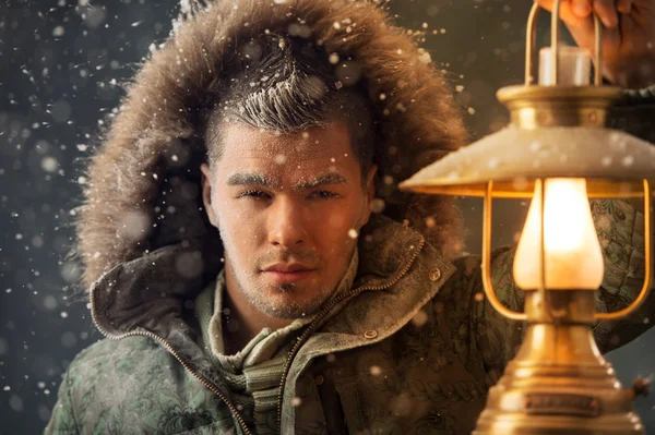 Brutal homem caminhando sob tempestade de neve à noite iluminando seu caminho com lanterna — Fotografia de Stock