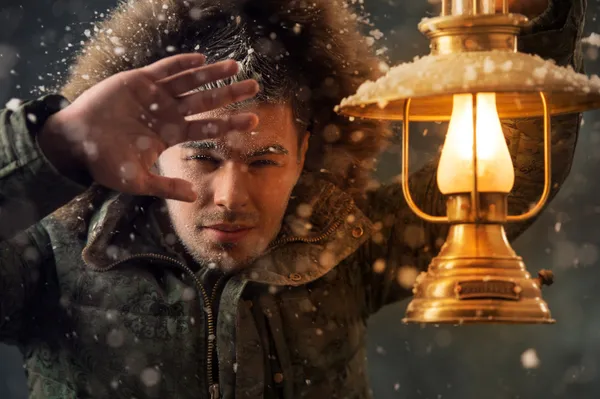 Brutal man walking under snowstorm at night lighting his way with lantern — Stock Photo, Image