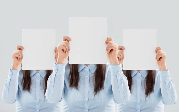 Three women showing blank paper sheets in front of their heads — Stock Photo, Image