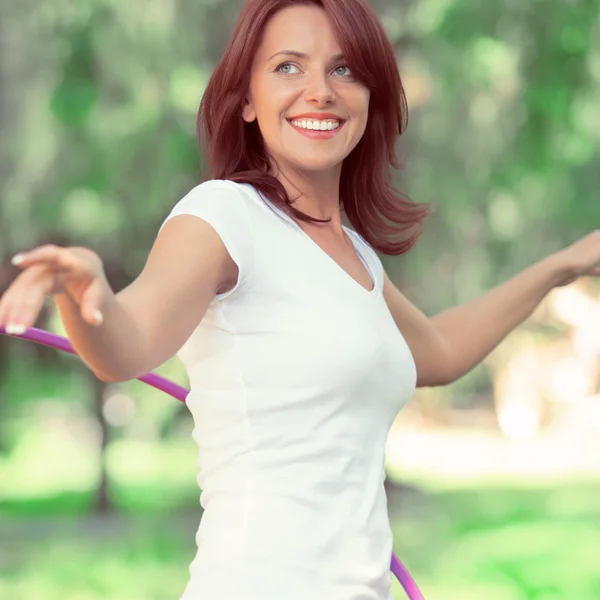 Woman rotates hula hoop on nature background — Stock Photo, Image