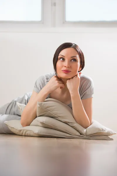 Mujer joven feliz acostada en el suelo con almohadas —  Fotos de Stock