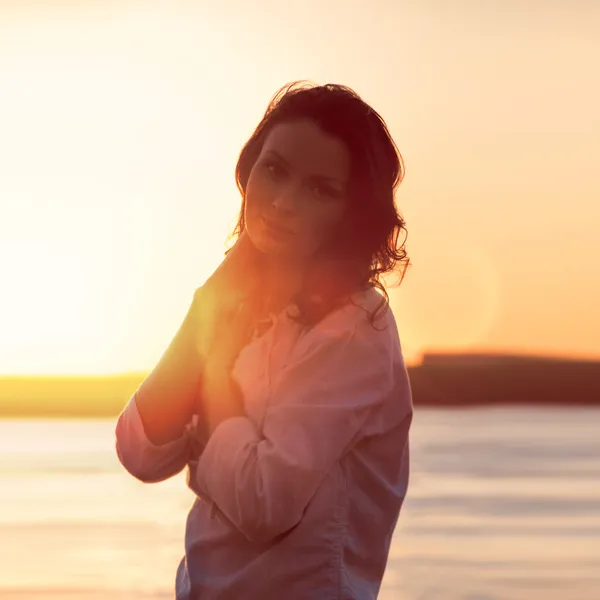 Jovem mulher andando na praia sob a luz do pôr do sol — Fotografia de Stock