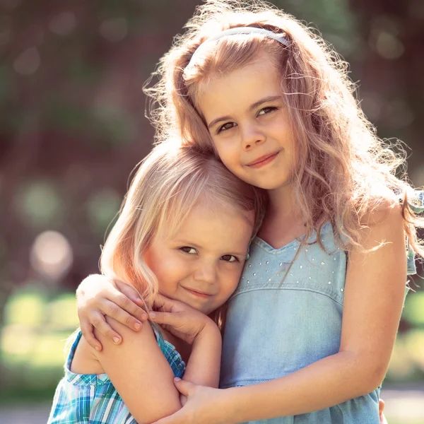 Внешний портрет двух обнимающих милых маленьких девочек — стоковое фото