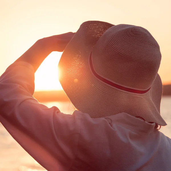 Mulher jovem e bonita usando um chapéu ao pôr do sol luz olhando — Fotografia de Stock