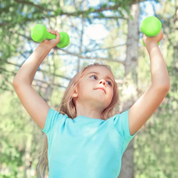 Happy little girl lifting dumbbells in park outdoors — Stock Photo, Image
