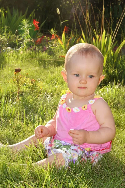 Baby girl sitting on the grass in the sun — Stock Photo, Image