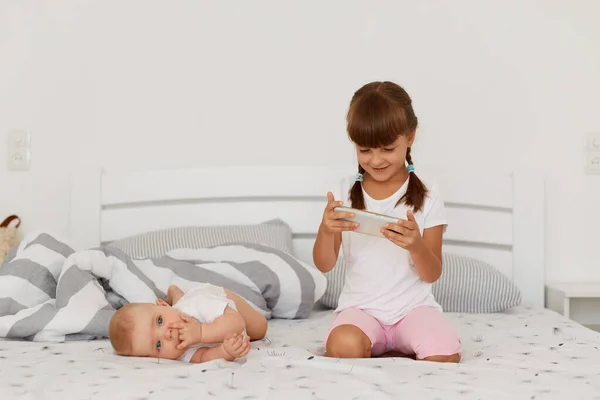 Işık Odasında Yatakta Poz Veren Iki Çocuk Akıllı Telefondan Çizgi — Stok fotoğraf