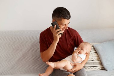 Pozitif siyah saçlı bir babanın portresi cep telefonuyla konuşuyor, küçük kızını elinde tutuyor, hoş sohbetler ediyor, çocuğuyla vakit geçiriyor..